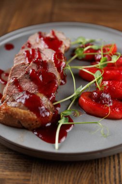 İyi sunulmuş bir tabakta, gri bir tabakta taze çileklerin yanında kırmızı sosla serpiştirilmiş et yer alıyor. Yemek canlı renkler ve dokular sergiliyor..