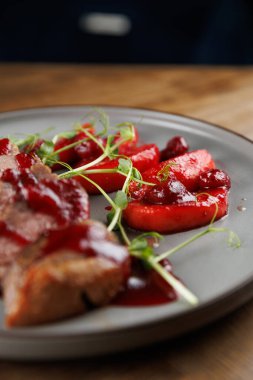 Bir tabak, bol soslu dilimlenmiş etin yanında yeşil sebzelerle süslenmiş taze kırmızı sebzeler sunar. Ortam sıcak, davetkar ve yemek için uygun..