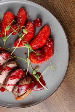 Bir tabak içinde kiraz soslu ve kırmızı meyveli ördek dilimleri var. Tabakta canlı renkler ve taze garnitür bir restoranda sunum için sergileniyor..