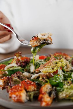 Bir insan, içinde sebze, sebze ve deniz ürünleri bulunan bir parça deniz ürünleri salatasıyla çatal tutar. Yemeklerin tadını çıkarırken ortam çok rahat..