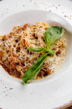 Bir porsiyon makarna üzerine rendelenmiş peynir ve beyaz bir kasede taze fesleğen konmuş et sosu içerir. Sıcak bir ortamda öğle ya da akşam yemeği için ideal..