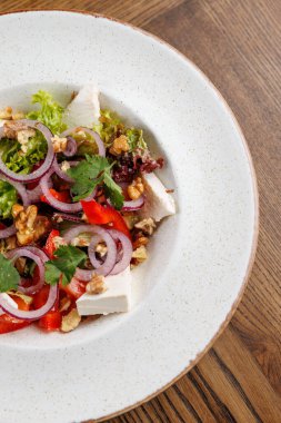 Renkli bir salata dilimlenmiş tavuk, marul, domates, soğan ve ceviz içerir. Kişniş ile süslenir ve ahşap bir masada yuvarlak bir tabakta sunulur..