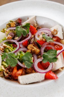 Renkli bir salata tabakası taze sebzeler, tavuk ve üzerinde dilimlenmiş soğan ve fındık. Bu yemek uluslararası mutfağın çeşitliliğini vurgular..