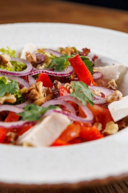 İçinde taze domates, kırmızı soğan, yeşil marul, dolma biber ve ceviz bulunan canlı bir salata dolu bir kase. Zevk almaya hazır basit ama renkli bir yemek..