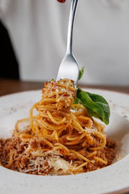 Çatal, et soslu spagetti servisini tabaktan kaldırır. Taze fesleğen ve peynir, zengin lezzetlerini vurgulayarak yemeği süslüyor. Sıcak bir ortam yemek deneyimini sarar..