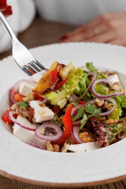 Bir el, salatadan bir ısırık almış çatalı canlı yeşiller, kırmızı biberler ve soğanlar olarak bir kasede düzenlenir. Bu yemek çeşitli mutfak geleneklerinden tatlar sergiliyor..