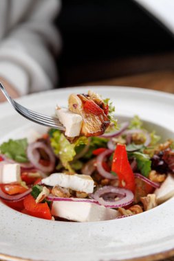 Restoranda bir kase salata servis edilir. Taze marul, tavuk parçaları, kırmızı soğan ve renkli sebzeler birleştirilir. Bir çatal salatadan bir parça tutar..