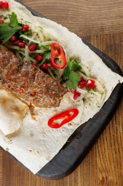 Lezzetli bir yemek sergisi taze otlar, dilimlenmiş sebzeler ve sıcak bir yemek ortamında ahşap bir tabakta nar tohumlarının yanında baharatlı et sunar..