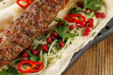 Bir yemekte taze bitkilerle ızgara kebaplar, dilimlenmiş soğanlar, nar tohumları ve kırmızı biberler yer alır. Her bileşen yemeğe renk ve doku ekler..