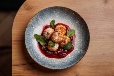 Taze yapılmış meyveli börekler, nane yapraklarıyla süslenmiş canlı böğürtlen sosunun üzerine oturur. Bu yemek çeşitli yemek etkinlikleri için uygun renkli bir sunum sunar..