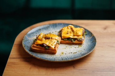 Lezzetli waffle 'lar erimiş peynir ve taze yeşilliklerle servis edilir. Tabak ahşap bir masaya konur. Kapalı bir ortamda, yemek için mükemmel..