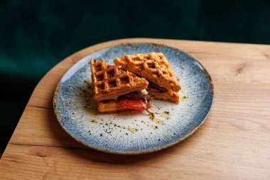 Waffles are sliced and filled with fresh vegetables on a plate. The dish showcases a unique take on traditional waffles in a cozy restaurant atmosphere.