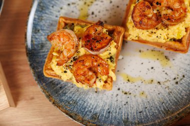 Shrimp and scrambled eggs are plated on a crisp base, garnished with black pepper. Enjoyed in a modern restaurant, this dish offers a tasty fusion experience.