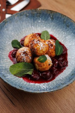 Kızarmış hamur köfteleri, altında kiraz sosu olan bir tabağa konur. Taze nane yaprakları renk katar. Bu yemek lezzet ve sunumun bir karışımını sergiler.