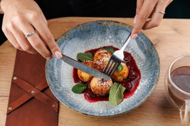 İki el, nane yapraklarının yanında canlı bir sosun üzerinde duran bir tabak hamur köftesinin üzerinde çatal ve bıçak tutuyor. Masada sıcak bir içecek var..
