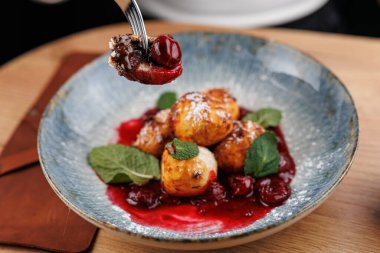 Hamur köfteleri böğürtlen sosuyla kaplanır ve mavi tabakta nane şekeri ile süslenir. Çatal, bir hamur köftesini kaldırıyor, eğlenmeye hazır. Ortam sıcak ve davetkar..