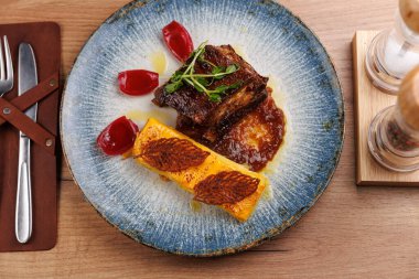 Bir tabak sosla ızgara et ve renkli elementlerle süslenir. Ayarlar, detaylara dikkat ederek küresel mutfağın çeşitliliğini vurguluyor.