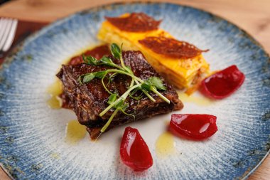 Bir yemek tabağında bir porsiyon sığır eti, katmanlı sarı pasta ve mavi bir tabakta kırmızı jöle bulunur. Yemek taze otlarla süslenir ve sosla süslenir..