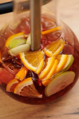 Renkli bir içecek içinde portakal, limon ve greyfurt dilimleri. İçki imalatçısı sıradan bir mutfakta ahşap bir tezgahın üzerinde oturur. Taze meyve içeceğe tat ve enerji katar..