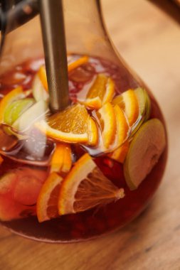Renkli meyve sangria ile dolu cam sürahi zengin bir sıvıya batırılmış portakal, limon ve diğer meyveleri gösterir. Sahne, serinletici içeceği servise hazır hale getirir..