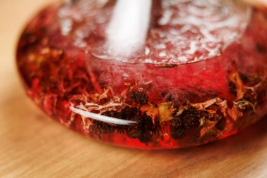 Bir cam kap kurumuş çiçeklerle harmanlanmış canlı kırmızı bir sıvı tutar. Tasarım, mutfak sunumunda yaratıcılığı göstererek, yiyecek ve içecek gösteriminin sanatsal tarafını vurgular..