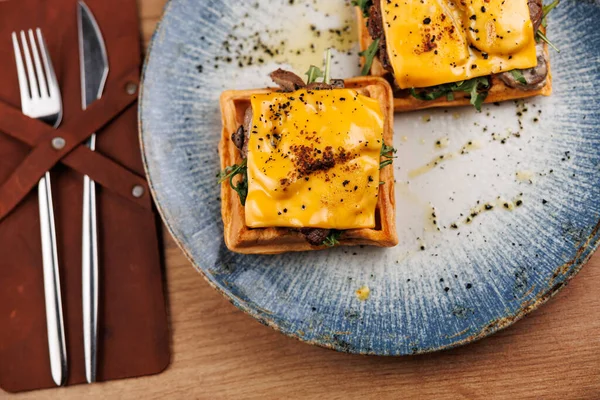 Tabaklar birden fazla mutfaktan çeşitli malzemeler ve stiller sergiliyor. Bir tabakta iki porsiyon peynir ve et var, ahşap bir masada yeşilliklerle tamamlanmış..