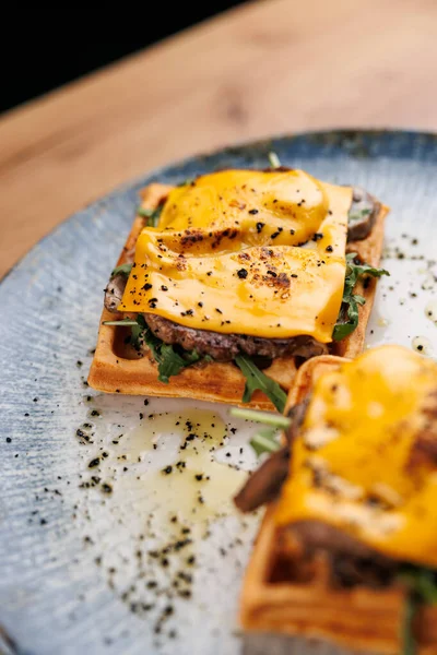 Peynir, sığır eti ve roka katmanlı waffle 'lar dekoratif mavi bir tabakta sunulur. Taze bitkiler ve zeytinyağı sağlıklı bir yemek için tabağı güçlendirir..