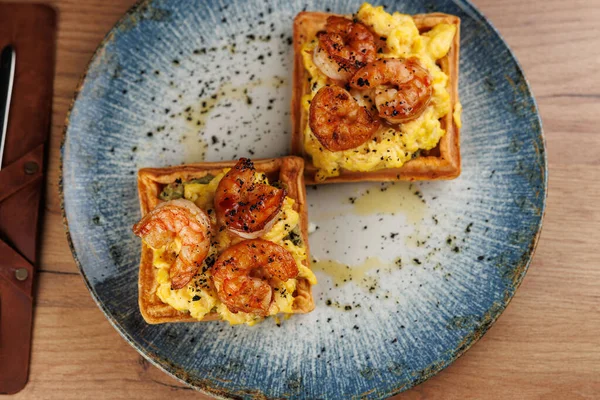 Üzerine çırpılmış yumurta ve karides konmuş iki kare waffle mavi bir tabakta oturur. Öğleden sonra sıcak bir lokanta var. Yemeklerini yemeleri için davet ediyorlar..