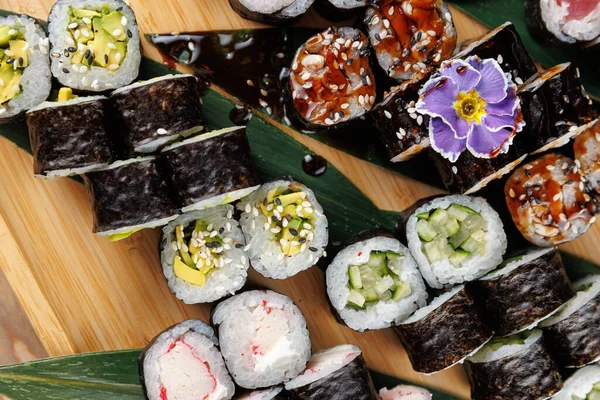 Suşi ruloları ahşap bir tahtada ustalıkla düzenlenir. Çeşitli türlerin dokuları ve renkleri vurgulanıyor, mutfak işçiliğini gösteriyor.