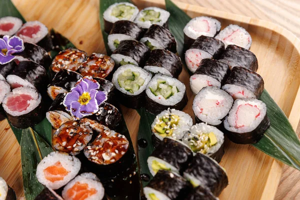 Bu ekran, pirinç, yosun ve farklı dolgulardan oluşan renkli bir suşi çeşidi sunar. Suşi ahşap bir tabakta dekoratif yapraklarla güzelce düzenlenmiştir..