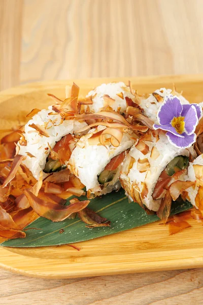 Suşi ruloları, sebzelerle dolu, çıtır çıtır soslar ve çiçeklerle süslenmiş ahşap bir tabakta düzenlenir. Yemekler lezzet ve dokuların karışımını sergiliyor..