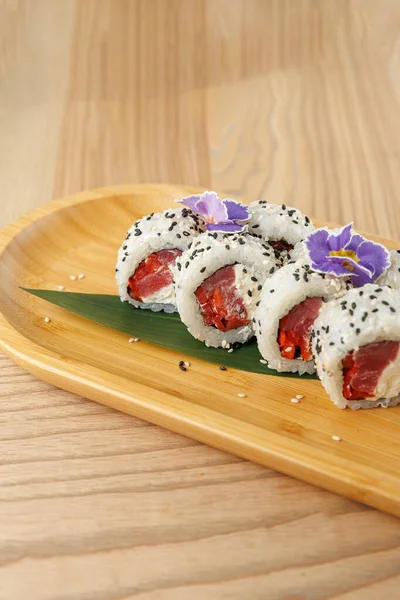 Taze ton balığından yapılmış suşi ruloları ve pirinçle sarılmış olarak ahşap bir tabağa konur. Yenilebilir çiçekler ve susam tohumları özel bir dokunuş ekler. Aydınlık ve davetkar bir ortam..
