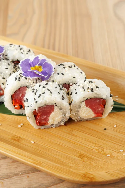 Taze balık ve sebzelerle dolu suşi ruloları ahşap bir tabakta güzelce düzenlenir. Güzel bir çiçek sunuma dekoratif bir dokunuş ekler. Yemek ya da toplama için mükemmel..