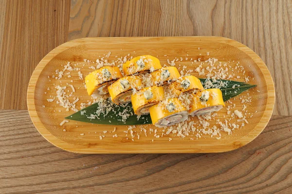 Renkli suşi dürümleri, yakınlarda çubuklar olan ahşap bir tabağa konur. Öğütülmüş malzemeler üzerine serpilmiş. Bu da yemeklerin gelişigüzel bir restoranda sunulmasını sağlıyor..