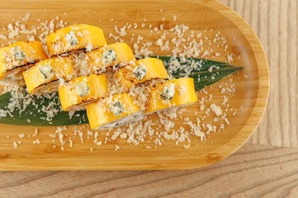 Suşi, sarı peynir ve yengeç ile birlikte ahşap bir tabakta oturur. Ekmekler rendelenmiş peynirle süslenir ve sunum için bir yaprağa yerleştirilir..