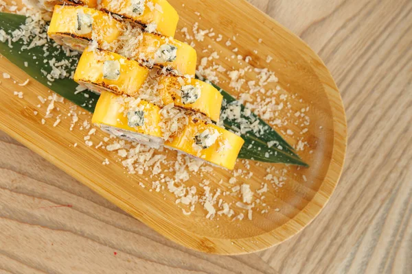 Suşi ruloları bambu bir tabakta ince bir garnitür ile güzelce düzenlenir. Tabakta parlak renkler ve geleneksel Japon tatları sergileniyor..