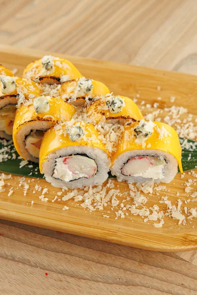 Suşi ruloları ahşap bir tahtanın üzerinde düzenlenir. Ekmekler yengeç, krem peynir ve çeşitli süslemelerle kaplıdır. Bu ayar sıradan bir yemek deneyimi sunuyor..
