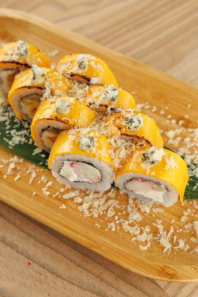 Suşi ruloları ahşap bir tabakta, canlı renkler ve dokular sergilenerek güzelce düzenlenir. Bu yemek Japon mutfak sanatını yansıtan malzemelerin karışımını vurgular..