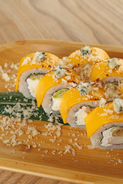 Suşi dürümleri ahşap bir tepside hazırlanır, üzeri renkli malzemeler ve süslemelerle kaplıdır. Tabak sunumu ve detaylara odaklanarak, ortam gündelik..