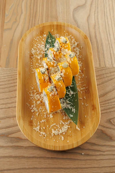 Suşi ruloları ahşap bir tepside, balık gevreğiyle süslenmiş ve taze yapraklara yerleştirilmiş. Bu yemek Japon mutfağını gösteriyor..