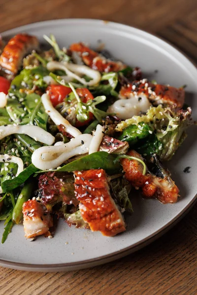 Bu yemekte yuvarlak tabakta ızgara yılan balığı, taze sebze ve erişte karışımı yer alıyor. Parlak renkler ve dokular sergiliyor, lokantaları benzersiz bir yemeğe davet ediyor..