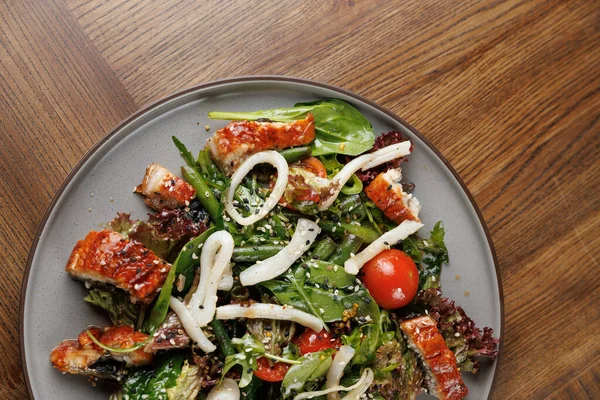 Bu yemekte taze yeşillikler, ızgara balık parçaları, kiraz domatesleri ve yuvarlak tabakta servis edilen dilimlenmiş soğanlardan oluşan renkli bir salata yer alıyor. Çeşitli dokuları ve tatları vurguluyor..