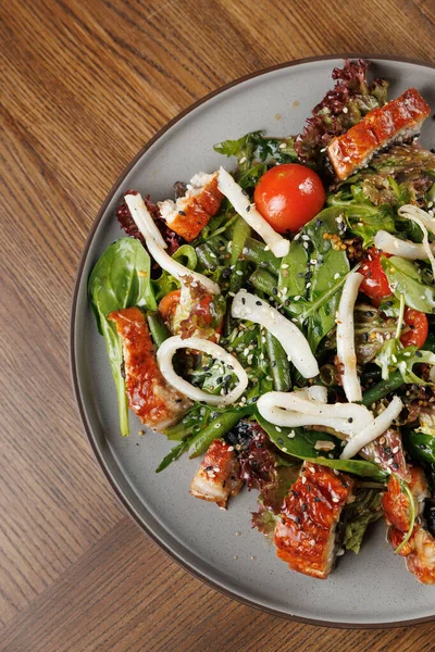 Bir kasede yeşil yapraklı taze bir salata, kiraz domatesleri ve ahşap bir masaya dizilmiş ızgara balık parçaları var. Lezzetli bir yemek deneyimini davet ediyor..