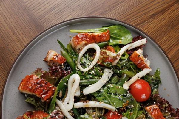 Tabakta taze ıspanak, ızgara tavuk, kiraz domatesleri ve susam tohumundan oluşan renkli bir salata sergileniyor. Salata, rahat bir atmosferde, ahşap bir masaya konur..