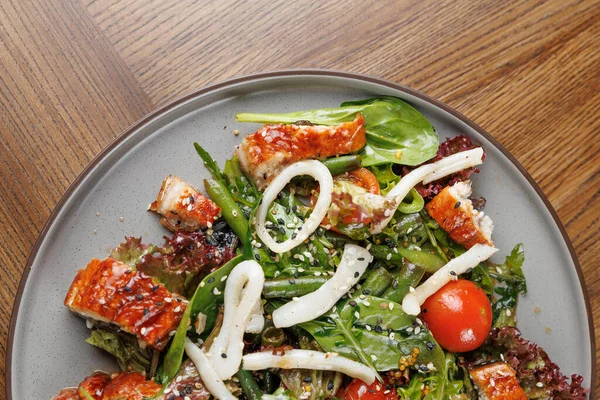 Izgara tavuk parçaları, kiraz domatesleri ve yuvarlak bir tabakta sunulan çeşitli yeşilliklerin yer aldığı renkli bir salata. Dekor, yemeğin tazeliğini vurgulayan ahşap bir masa gösteriyor..