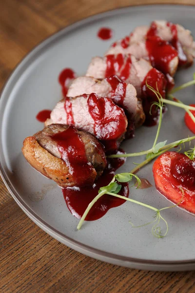Sos serpiştirilmiş et dilimleri yuvarlak bir tabakta oturur. Taze süslemeler ve domatesler yemeğe eşlik ediyor. Bu yemek, mutfak stillerinin bir karışımını sergiler..