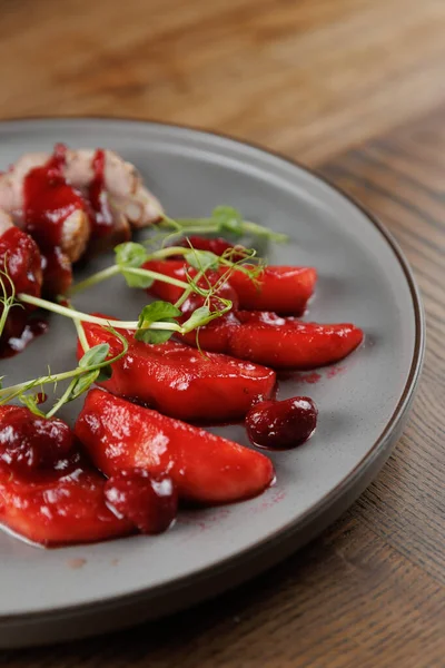 Bir tabak, parlak kırmızı sos, meyve dilimleri ve yeşil süslemeler içeren Ukrayna ve Japon mutfağının bir karışımını sergiliyor. Ayar, ahşap bir masa bitiş noktasını vurguluyor..