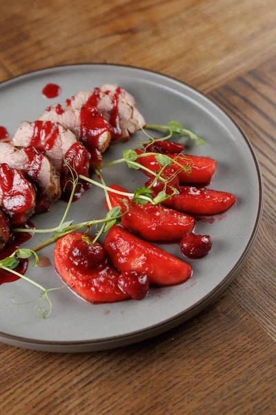 Kızarmış et dilimleri üzerinde kırmızı sos bulunan gri bir tabakta düzenlenir. Etin yanında kiraz yarımları ve taze yeşilliklerle süslenir..