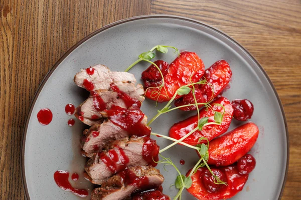 Tabakta, basit bir tabakta kavrulmuş kırmızı biberle birlikte kiraz soslu dilimlenmiş ördek yer. Taze yeşillikler renk katar.
