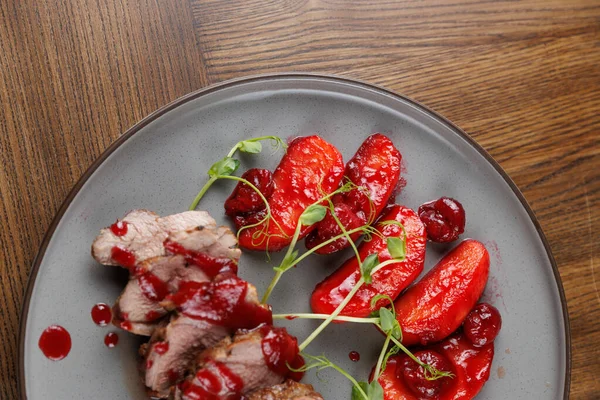 Dilimlenmiş et bir tabakta soslu meyvenin yanında düzenlenir. Yemek çeşitli mutfaklarda tipik lezzet karışımının altını çiziyor. Ayarlar ahşap masa detaylarını gösteriyor.